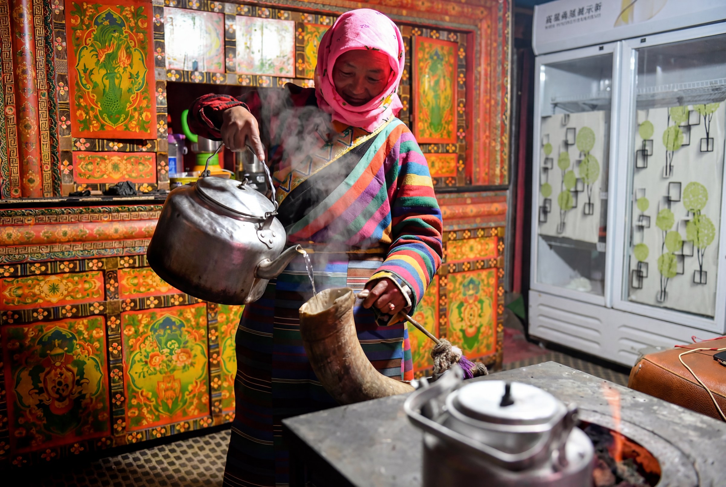 A Tibetan host pouring hot water into a traditional vessel inside a family home on Tagong Grassland